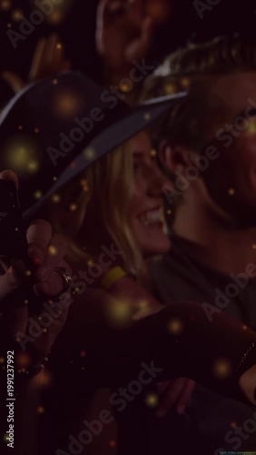 Vertical video: Woman in hat leaning, phone catching music light to record and gold dust over crowd