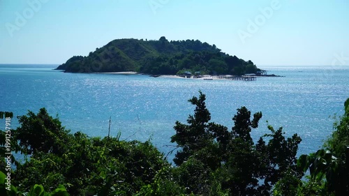 Small Tropical Island with Wooden Pier and Sandy Beach Viewed Through Lush Green Trees Over Calm Blue Sea - 4K Footage