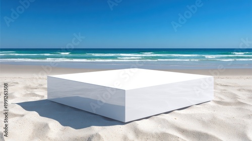 White cube on sandy beach under clear blue sky with ocean background
