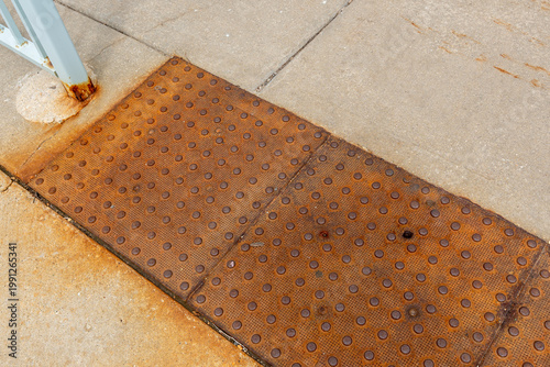 Close-up of a rusty iron platform with raised bumps on asphalt, designed to assist visually impaired individuals, ensuring safe navigation on the ground