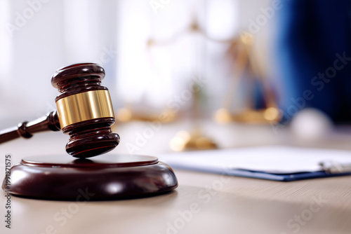 Wooden judge gavel on desk with blurred scales of justice and legal documents, law and courtroom authority concept