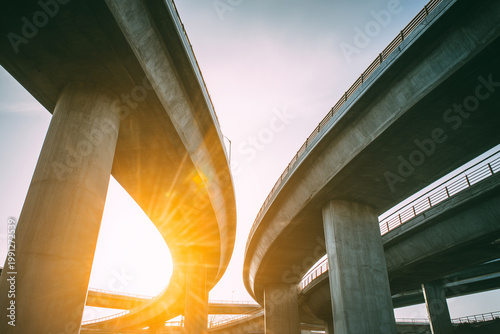 Low angle view of concrete highway overpass and curved flyover bridge at sunset, modern urban infrastructure and transport concept