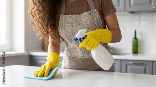 Woman in apron cleaning kitchen countertop with spray and cloth