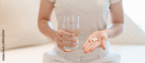 Obraz na płótnie woman hand holding medicine painkiller pill and water glass on the sofa at home,