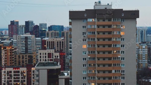 Getting dark and modern residential buildings turn on lights in apartments. High-angle view timelapse