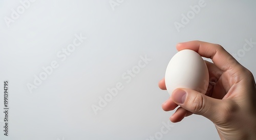Hand holding a fresh white chicken egg on a neutral background