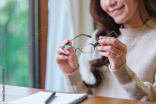 Closeup image of a woman holding glasses while writing on notebook at home