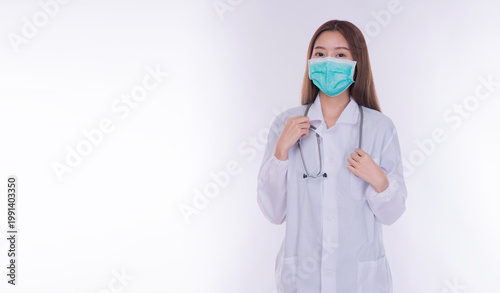 Professional young Asian female doctor wearing a white lab coat, medical face mask, and stethoscope looking at camera. Isolated on white background with copy space. Healthcare and medical concept.