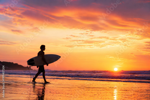 Surfer walking with surfboard at sunset, summer adventure and ocean lifestyle