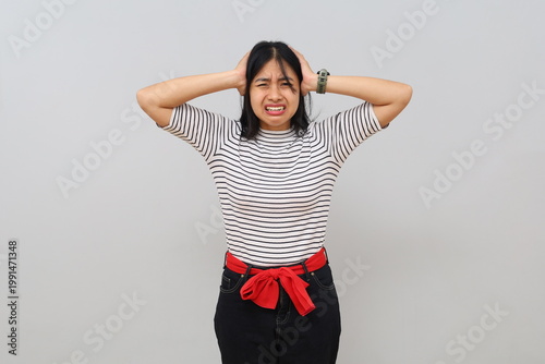 Canvastavla A young woman stands alone on a white background, looking angry, covering her ears with her fingers and screaming