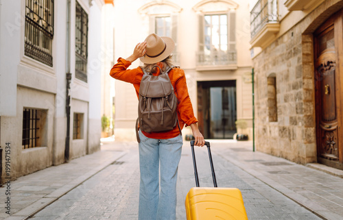Foto A woman walks along a narrow street, pulling a bright yellow suitcase