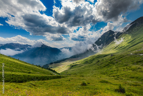 A lush green alpine meadows under a cloudy sky at the Colle delle Finestre mountain pass in Piedmont, Italy.