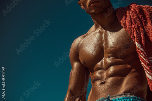 Handsome shirtless bodybuilder man with a muscular torso and fit abs poses with a black towel as a strong athlete showcasing his bodybuilding fitness and healthy muscles