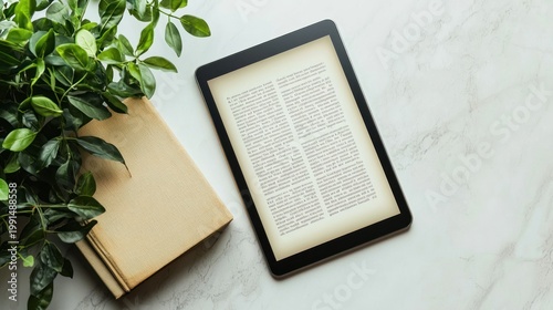 A digital tablet displays a page of an old book. A green plant sits beside the tablet on a white marble surface.