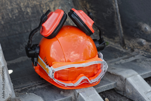 Fotografía Orange hard hat with protective goggles and hearing protection earmuffs placed on construction machinery