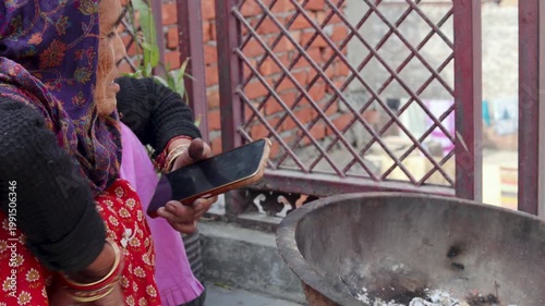 An Indian village woman holds a mobile phone while standing near a traditional cooking stove, capturing a blend of modern technology and rural daily life in a simple household setting