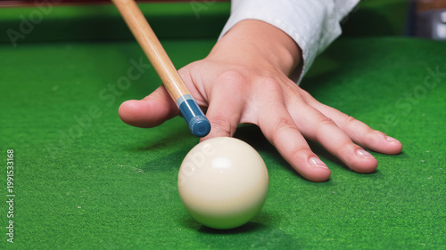 Close up of hand aiming cue at white billiard ball on green table, preparing precise shot in pool game. Leisure activity and skill practice in recreational environment