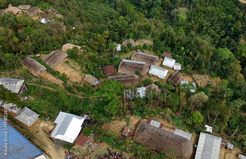 An aerial view of a rural village in Nagaland, India, traditional thatched houses and tin-roofed structures are scattered along forested slopes, connected by narrow paths