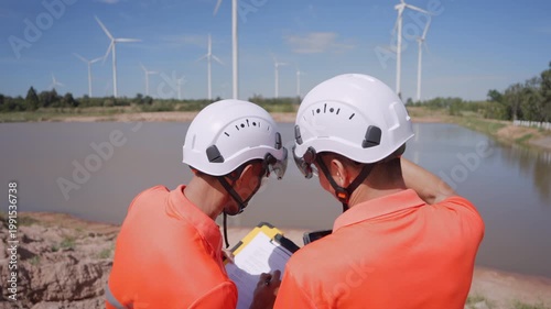 Close-up of Asian engineers using a tablet to inspect wind turbines at a renewable energy site, representing clean energy operations and sustainable technology use.