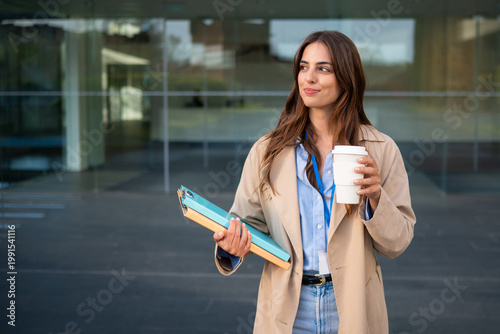 Professional woman carrying documents and coffee walking outdoors