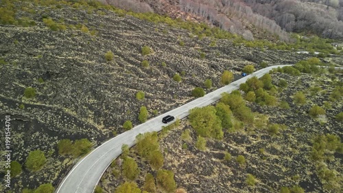 Black car navigates winding road through volcanic landscape, surrounded by green shrubs and rocky terrain, showcasing the beauty of nature and driving experience