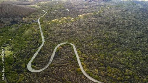 Aerial view of winding road through volcanic landscape with lush green vegetation and rocky terrain, showcasing the natural beauty of the region