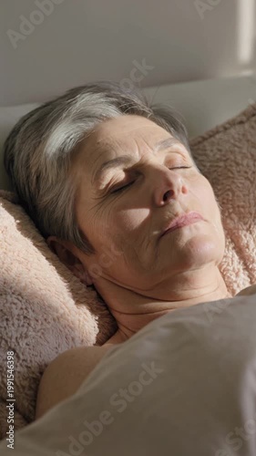 Senior woman sleeping peacefully in bed with morning sunlight, vertical shot