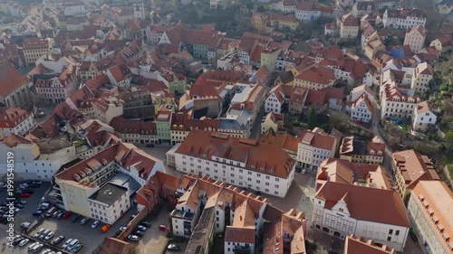 Bird's-eye view of the medieval old town of Meissen. The image shows the dense network of red tiled roofs, historical buildings, and winding alleys in warm daylight.