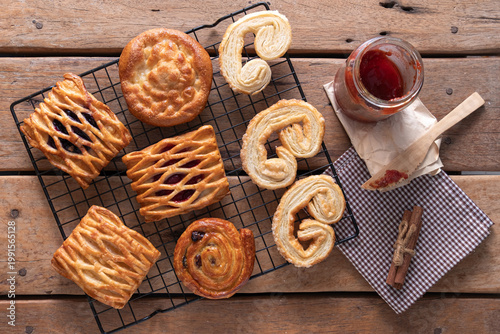 Assorted fresh Danish pastries and palmiers on a cooling rack over a wooden table.