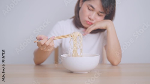 Bored young Asian woman eating instant noodles at home. Exhausted female looking unhappy while eating bowl ramen. quick meal after work, burnout and unhealthy eating habit, lifestyle and cheap meal