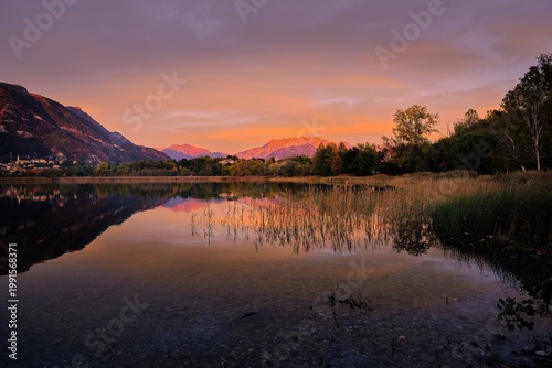 Vibrant sunset colors reflecting on Lake Pusiano with silhouettes of trees, Lombardy, Italy