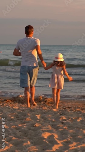 Back view of father and little daughter run on sand beach to sea at sunset. Summer vacation travel holiday. Vertical shot