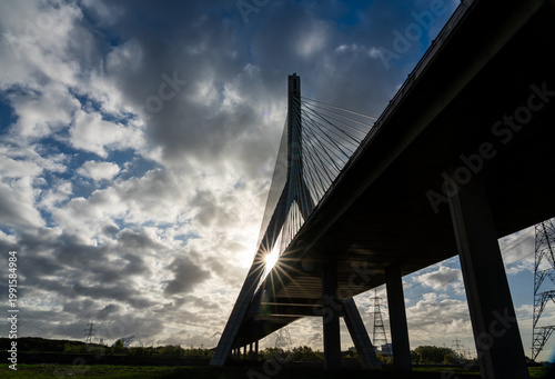 Flintshire Bridge pylon and stay cables silhouetted against a blue sky with dramatic clouds, a sunstar bursting through the bridge deck