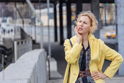 Fotografía Concerned woman in yellow coat touching face and thinking about problem in city