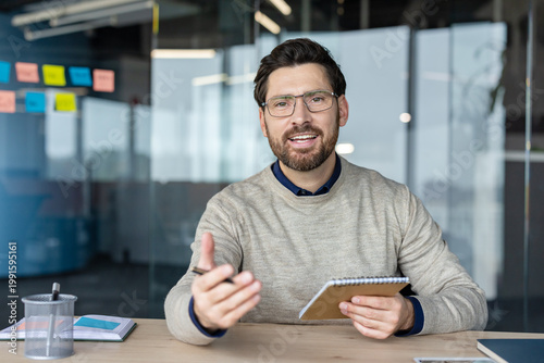 Smiling business professional using a notepad while participating in an online meeting, looking at the camera and explaining a business concept during a remote work conference