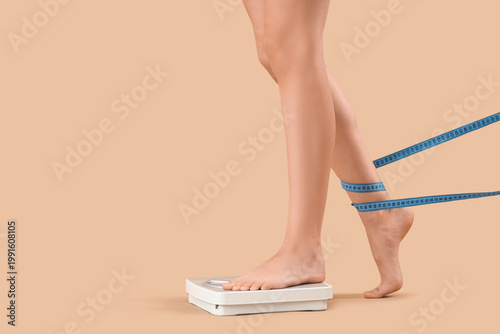 Foto Woman's legs with tape measure and weight scales on beige background