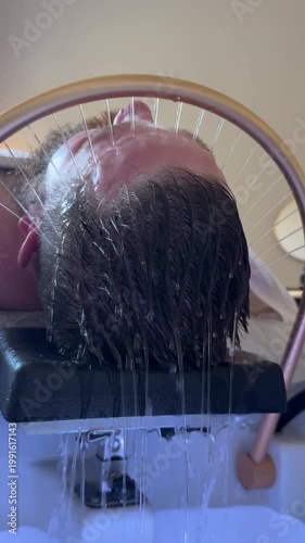 Close-up of Bearded Man receiving a head massage during a Japanese head spa treatment with water flowing from a special hair washing tool, focusing on the scalp relaxation and beauty therapy