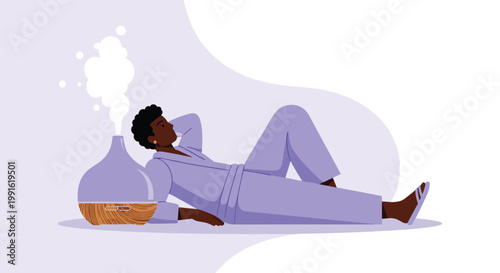 A relaxed person wearing a soft purple robe lies comfortably on the floor beside a modern wooden essential oil diffuser releasing a gentle white mist.