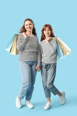 Beautiful young woman with her cute daughter holding shopping bags on blue background. Mother's Day celebration