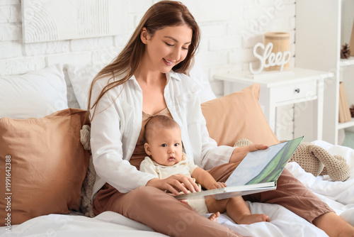 Mother with her baby reading book on bed at home