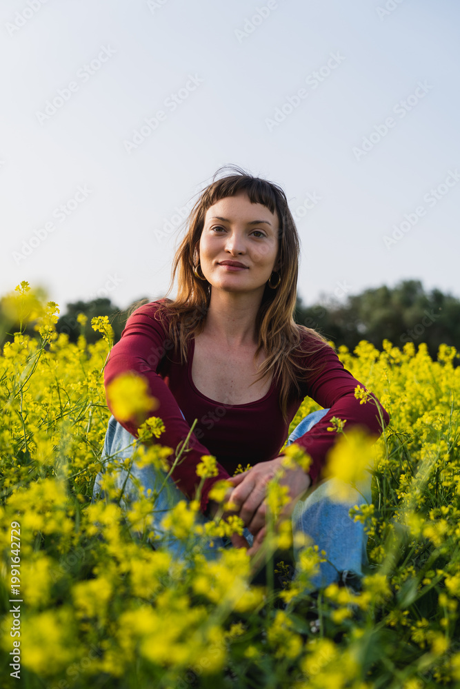 Fototapeta premium Woman smiling sitting in field of yellow flowers during spring