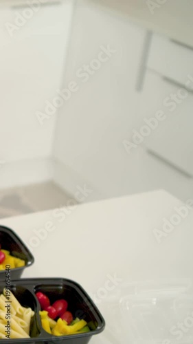 Vertical video: Reaching toward pink bowl hands adding tomatoes into boxes for meal prep, watch