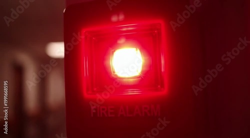 Close-up of a red fire alarm strobe flashing in a hallway, signaling danger with urgent light.