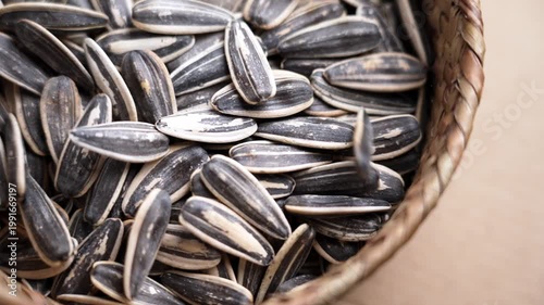 Roasted unpeeled sunflower seeds filling a rustic wicker basket in slow motion. Black and white striped texture of the shells. Healthy nutrition ingredient. Top view