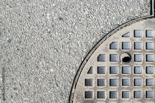 Fotografija Round metal manhole cover on rough asphalt surface with geometric city texture background