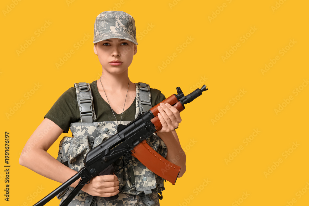 Fototapeta premium Confident young female soldier with assault rifle on yellow background