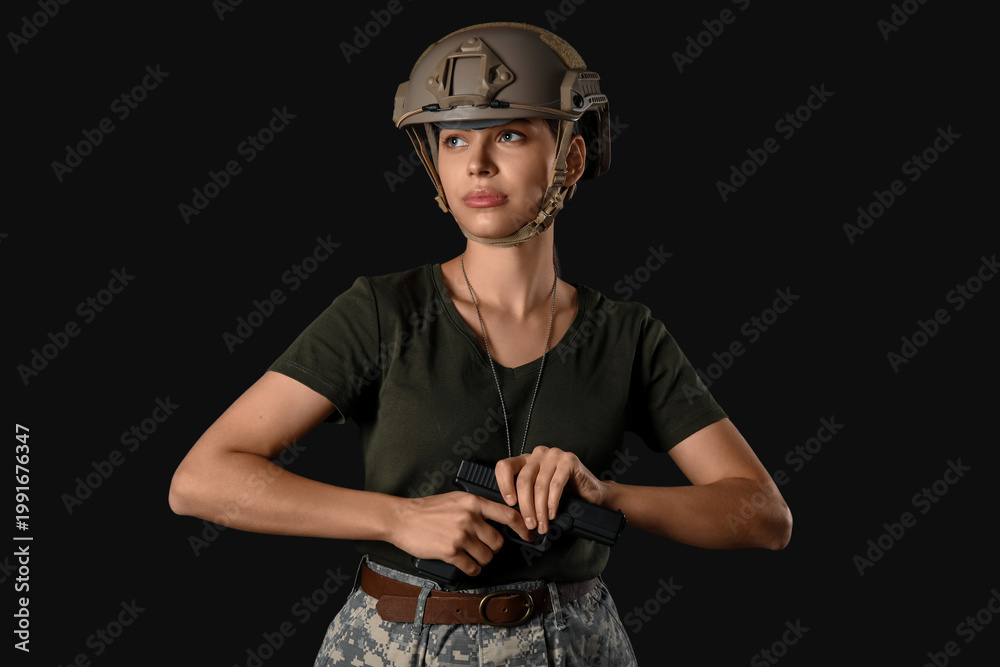 Fototapeta premium Confident young female soldier with handgun on black background