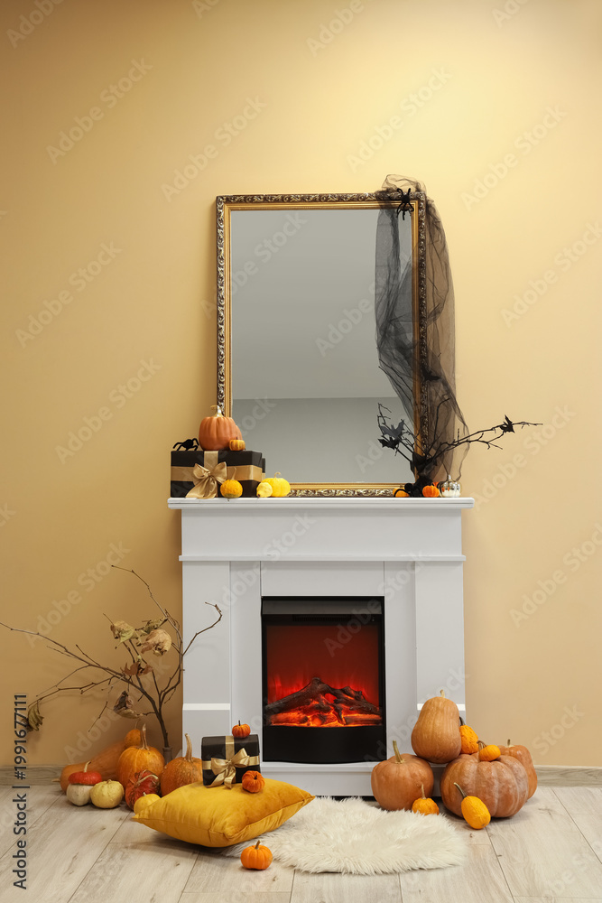 Fototapeta premium White fireplace with pumpkins, Halloween decor and mirror near yellow wall