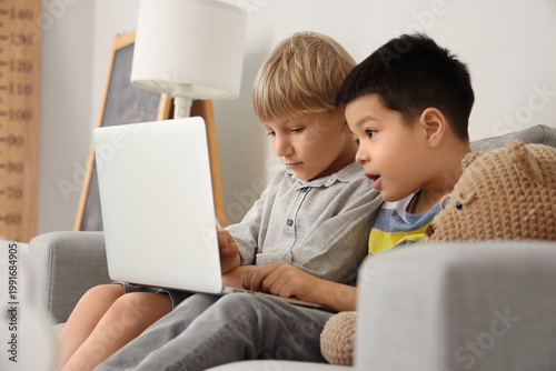 Cute little boys playing computer game on laptop at home