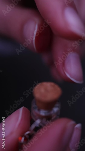 An extreme vertical close-up of a person's fingers carefully pushing a cork lid into a tiny glass jar to close it, emphasizing fine motor skills and tactile texture